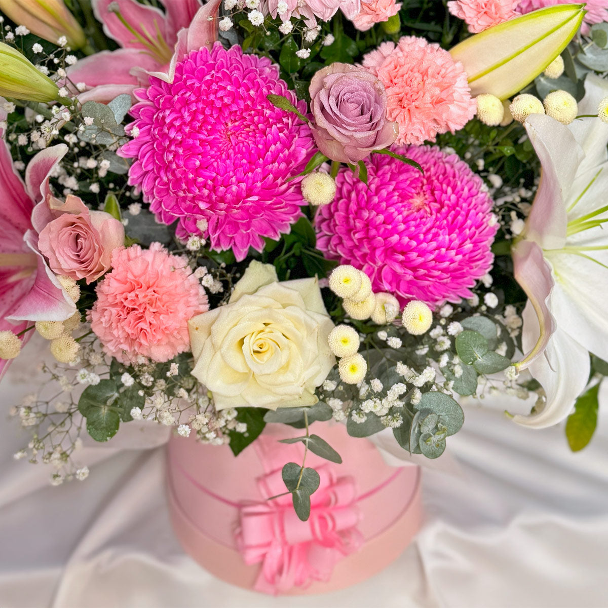 Roses, chrysanthemums and lilies in a pink flower arrangement in a pink hatbox