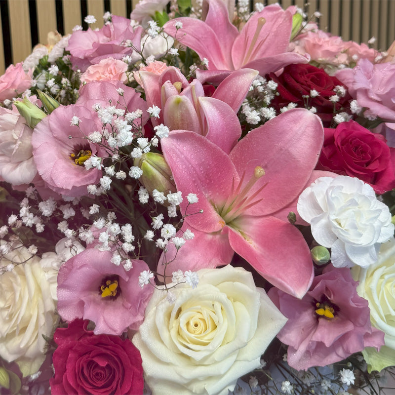 A breathtaking floral arrangement featuring pink lilies, white and red roses, and baby's breath in an elegant keepsake vase.