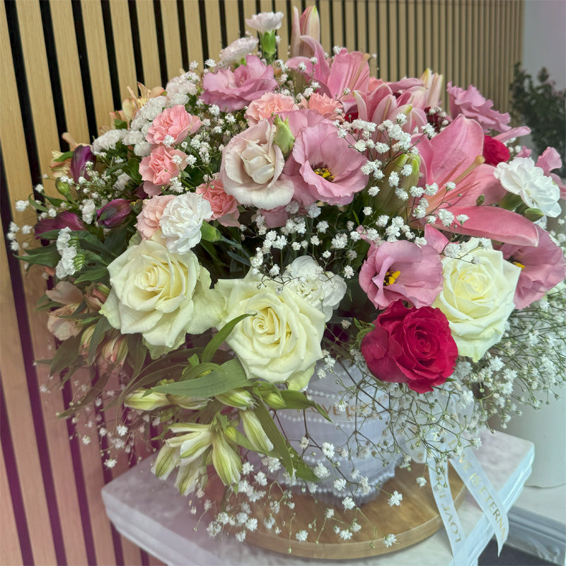 A luxurious floral display of soft pink lilies and premium roses, artistically arranged with delicate baby’s breath in a stylish white vase.